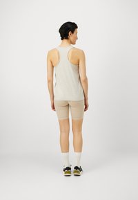 Svijetlosiva majica bez rukava s dizajnom racerback u kombinaciji s bež biciklističkim šortsevima. Model stoji okrenut leđima prema kameri, prikazujući minimalne šavove i glatku teksturu.