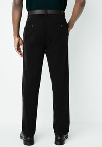 Sorte bukser med en afslappet pasform, der har en glat tekstur, to baglommer og et læderbælte. Båret med sorte sko.