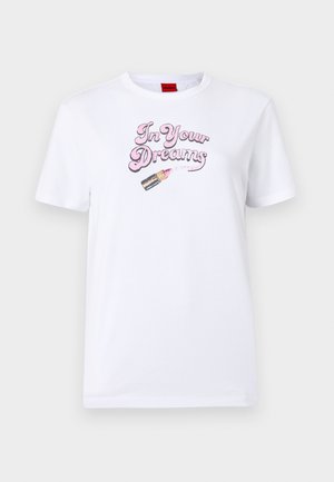 T-shirt bianco in cotone con la frase "Nei tuoi sogni" in carattere corsivo rosa e una grafica di un tubetto di rossetto con dettagli rosa.
