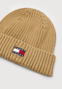 Beanie a coste color sabbia con risvolto, caratterizzato da una patch rettangolare del logo Tommy Jeans nei colori blu, bianco e rosso.