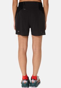 Black athletic shorts with a textured design, elastic waistband, and side pockets, paired with layered sports shoes and red socks.