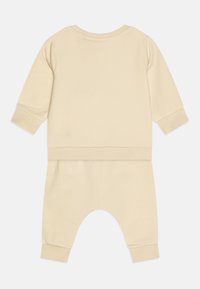 Light beige toddler tracksuit featuring a round neckline, long sleeves, and ribbed cuffs. The pants have a relaxed fit and elastic waistband.
