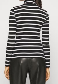 Zwart-wit gestreepte lange mouw top met een geribbelde textuur en een hoge hals, gecombineerd met zwarte, high-waisted, lerenachtige broek.