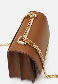 Bruine leren crossbody tas met gouden kettinghandvat en gouden hardware, met zichtbare zijcompartimenten en merkplaatje.