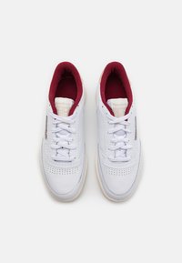 Weiße Ledersneaker mit einem gepolsterten burgunderroten Innenfutter, schnürbarem Verschluss, perforierter Zehenpartie und einer cremefarbenen Gummisohle. Logo auf der Zunge.