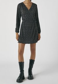 Robe noire à manches longues, ornée d'un motif à pois blancs et dotée d'un décolleté en V. Associée à des bottes de combat noires à lacets.