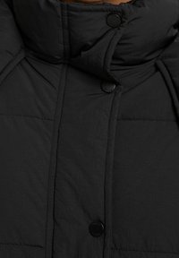 Svart puffjacka med hög krage, stilren quiltad textur och svarta knappar. Enkel, funktionell design med minimal detaljer.