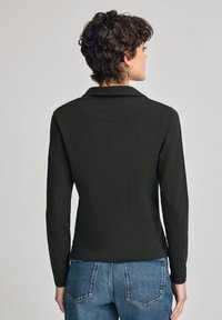 Long-sleeve polo shirt in dark green, featuring a collar, smooth texture, and a fitted design. Back view displays minimalist style.