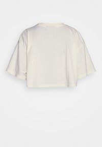 Kreeminvärvi lõhikud t-särk, lühikeste varrukatega, ümmarguse kaelusega, pehme puuvillase tekstuuriga ja minimaalsete õmblusdetailidega.