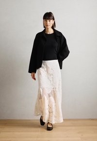 Black oversized jacket, fitted black top, long white lace skirt with floral pattern, and black flat shoes, on a light wooden floor.