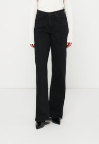 Czarne dżinsy z rozszerzanymi nogawkami i wysokim stanem, z przednimi kieszeniami oraz klasycznym zapięciem na guzik. Teksturowany materiał wprowadza subtelny detal.
