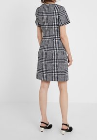 Robe à carreaux bleu marine et blanc avec manches courtes, taille ajustée et jupe évasée. Texture tissée, associée à des chaussures noires ornées d'accents en perles.