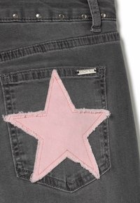 Vaqueros de mezclilla gris con un gran parche en forma de estrella rosa en el bolsillo trasero, con bordes deshilachados y una etiqueta metálica cerca de la pretina.