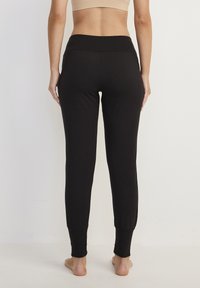Svarta leggings med en mjuk, elastisk textur och ett brett, elastiskt midjeband. Avsmalnande ben med åtsittande mudd vid anklarna.