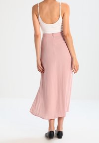 Jupe maxi fluide rose clair avec une texture lisse, une fermeture éclair à l'arrière et un ourlet légèrement évasé, associée à un débardeur blanc.
