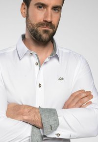 Weißes Hemd mit Strukturierung, grauem Kragen und Manschetten. Mit grünem Logo und Messingknöpfen an der Vorderseite und den Manschetten.