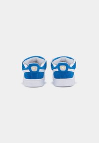 Une paire de baskets Puma bleues et blanches, en suède, montrées de l'arrière avec des logos Puma dorés sur les languettes des talons.