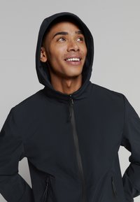 Zwarte hoodie met een gladde buitenkant, twee zijzakken met rits en een volledige rits aan de voorkant. Beschikt over een gestroomlijnd, modern ontwerp.