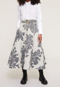 Floral patterned A-line skirt in cream and navy, featuring a wide waistband with a gold buckle, complemented by black lace-up boots.