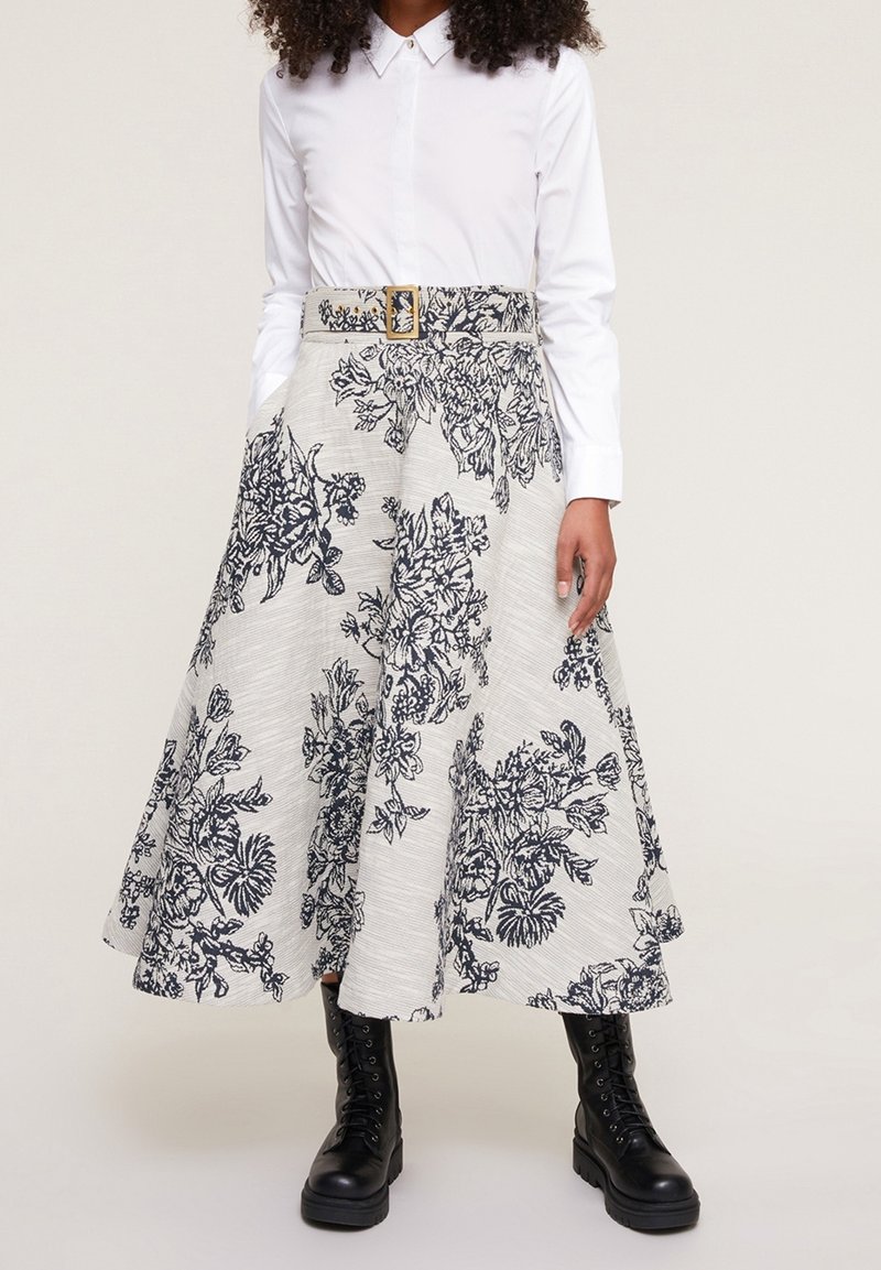 Floral patterned A-line skirt in cream and navy, featuring a wide waistband with a gold buckle, complemented by black lace-up boots.