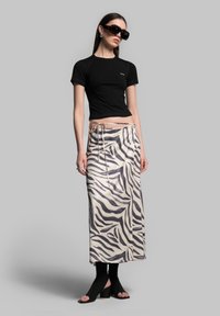 Black cropped t-shirt, zebra print maxi skirt in beige and gray, high-heeled black open-toe mules, and oversized black sunglasses.