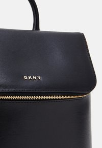 Czarny skórzany plecak o fakturowanej powierzchni. Posiada złoty suwak oraz metaliczne logo "DKNY" na klapce. Kompaktowy i strukturalny design.