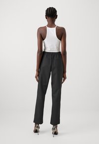 Černé kalhoty s elastickým pasem a rovnými nohavicemi, zdobené jemnou texturou, v kombinaci s bílým topem bez rukávů. Modelka má na sobě stříbrné lodičky.