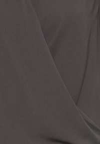 Tissu gris foncé avec une texture lisse et douce. Le matériau présente une légère élasticité, créant des sections drapées et superposées dans un design décontracté.