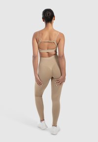 Reggiseno sportivo beige con schiena a taglio e spalline regolabili abbinato a leggings a vita alta con dettagli senza cuciture e una texture liscia.