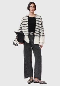 Overmaat gestreepte cardigan in crème en zwart, zwarte aansluitende top, versleten zwarte jeans, en zwart-witte gepatterneerde schoenen, met een zwarte tas.