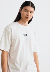 Kremfarget bomull t-skjorte med korte ermer, med en svart logo fra "The North Face" på brystet. Enkel, avslappet passform.