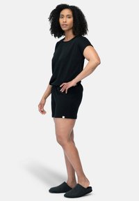 Zwart relax-fit short set van gestructureerde stof, met korte mouwen, een elastische taille en zwarte slipper-achtige schoenen.