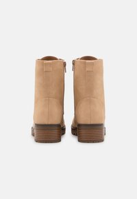 Beżowe botki do kostki wykonane z zamszu, z gładkim wykończeniem, zaokrąglonym noskiem, bocznymi zamkami błyskawicznymi oraz słupkowym drewnianym obcasem.