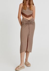Cropped top marrone con motivo e spalline sottili abbinato a una gonna di lunghezza media con davanti annodato e spacco, indossato con sandali chunky beige.