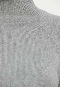 Grauer Strickpullover mit hohem Rippenrollkragen, weichem Stoff und dezenten Musterabweichungen über den Körper.