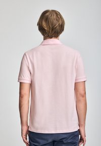 Lyserød polo-shirt med klassisk krave, korte ærmer og en blød tekstur. Synlig syning på ærmerne og et afslappet design.