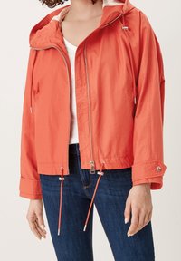 Leichte orangefarbene Jacke mit Reißverschluss vorne, Kordelzugverstellung am Saum und in der Kapuze sowie Druckknopfverschluss an den Ärmeln. Strukturierter Stoff, lässige Passform.