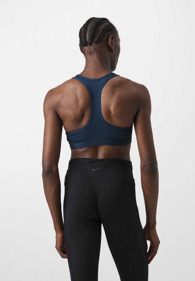 Soutien-gorge de sport bleu marine avec un dos nageur, en matériau extensible ; associé à un legging noir taille haute avec un logo à la taille.
