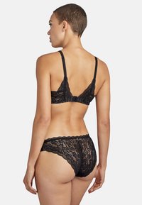 Bralette en dentelle noire avec des bretelles ajustables, une fermeture à crochet, et un bas assorti en dentelle avec un motif floral et des bords festonnés.