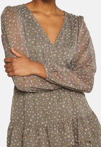 Robe à motifs floraux avec un décolleté en V, manches longues transparentes, en vert olive avec de petites fleurs roses et jaunes, dotée d'un ourlet à volants.