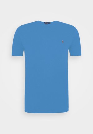 Niebieska bawełniana koszulka z krótkim rękawem, z okrągłym dekoltem i małym haftowanym logo po lewej stronie klatki piersiowej. Prosty wzór, gładka tekstura.