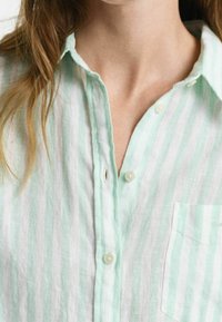Camisa abotonada a rayas verde claro y blanca con un bolsillo, que presenta un cuello con solapa y una textura de tela suave y ligera.