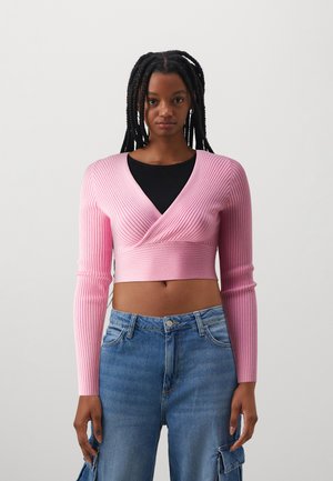 Top cropped rosa a coste con scollatura a V profonda e maniche lunghe, abbinato a pantaloni in denim blu con una vestibilità rilassata e tasche in stile cargo.
