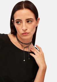 Sort perlekæde med knudedesign. Har metalliske detaljer og en struktureret overflade, der smukt hænger omkring halsen.