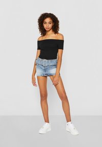 Top negru, fără umeri, asortat cu o fustă scurtă din denim de culoare albastră deschisă, având o curea lată. Modelul poartă adidași albi. Texturi netede.