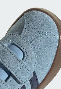 Chaussure pour tout-petit en daim bleu clair avec bride à velcro et semelle en caoutchouc marron, gros plan sur la zone des orteils montrant des coutures détaillées.
