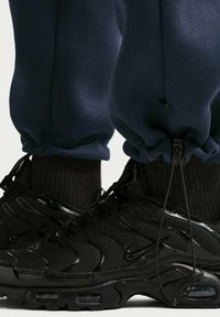 Μαύρα αθλητικά παπούτσια με υφή από πλέγμα και ελαστικά μέρη από καουτσούκ, που διαθέτουν κομψό σχέδιο. Μπλε σκούρα αθλητική φόρμα με ελαστικές μανσέτες και λεπτομέρεια με κορδόνι.