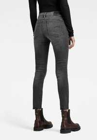 Jeans negros ajustados con cintura alta, presentando un dobladillo deshilachado y detalles de costura sutiles, combinados con botines de cuero marrón.