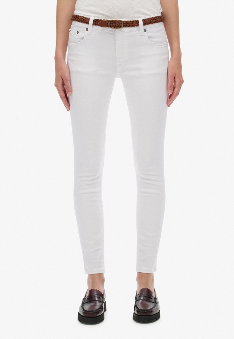 Jeans blancos ajustados de denim, con un cinturón trenzado marrón, bolsillos delanteros y un silueta entallada, combinados con mocasines oscuros.