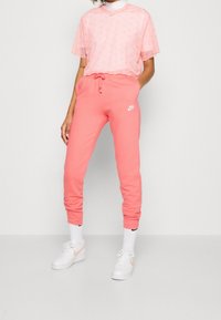 Rosa Nike t-shirt med subtilt mönster och logotyp, parat med matchande rosa sweatpants, med elastisk midja och ärmslut, bärs med vita sneakers.